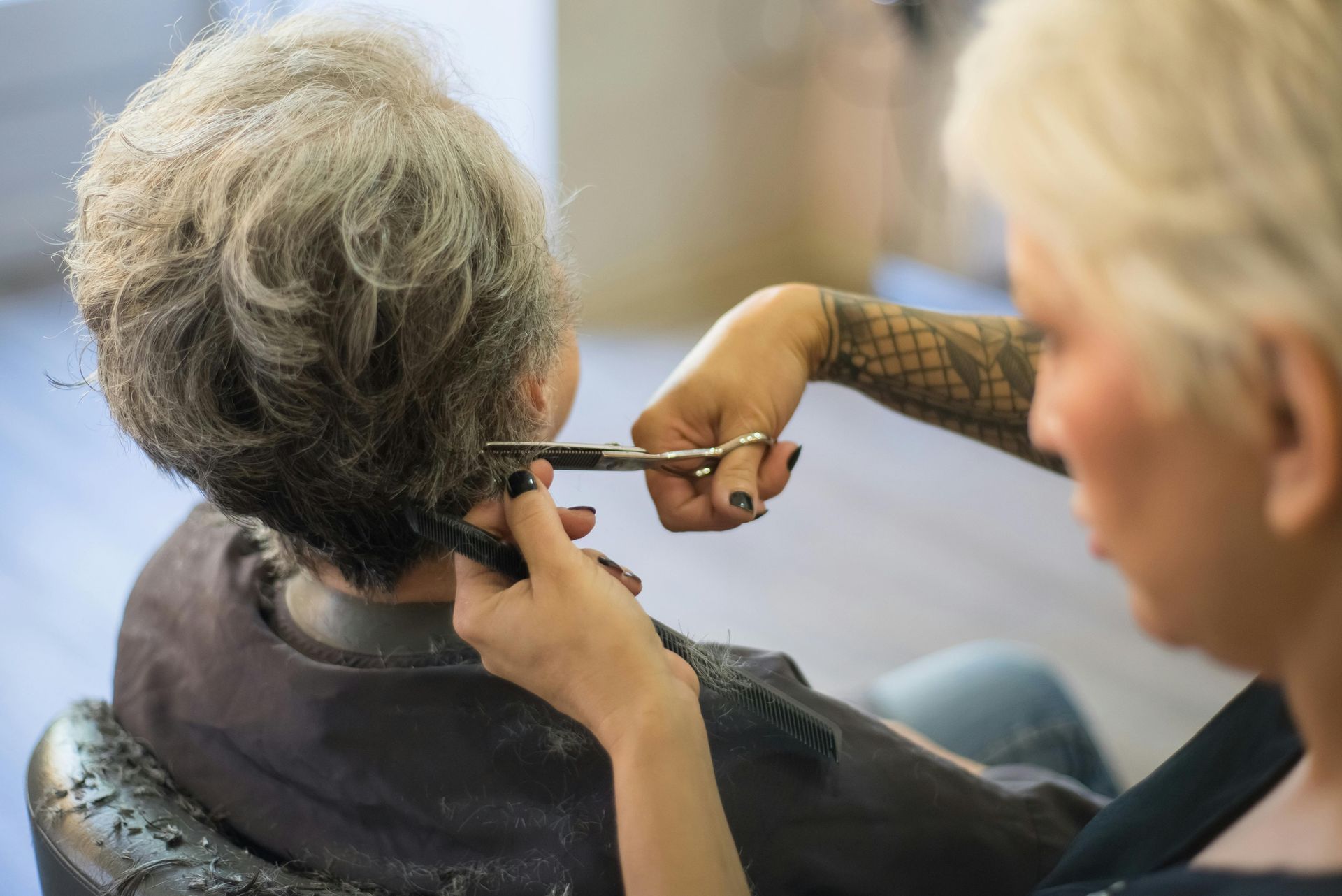 A stylist cuts the hair of a person seated in a salon chair, focusing on the back of the head.