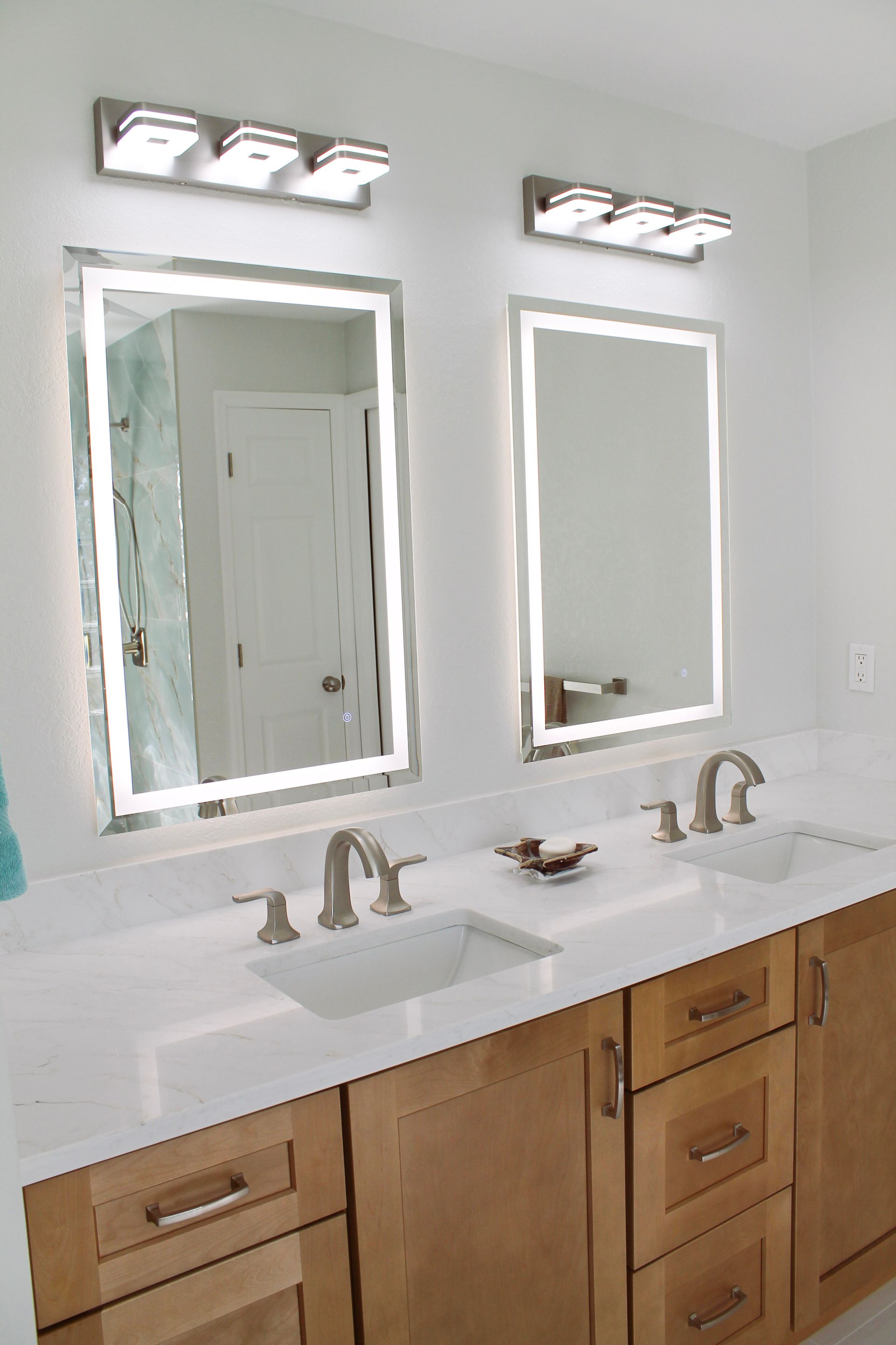 White Quartz countertop, with modern brushed stainless steel tap and handles, with white sink, Honey wood colored shaker cabinets with modern brushed silver handles and LED lit mirrors and brushed stainless steel modern lighting 