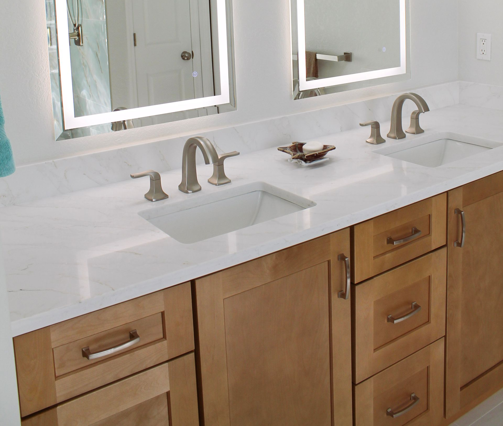 White Quartz countertop, with modern brushed stainless steel tap and handles, with white sink, Honey wood colored shaker cabinets with modern brushed silver handles and LED lit mirrors