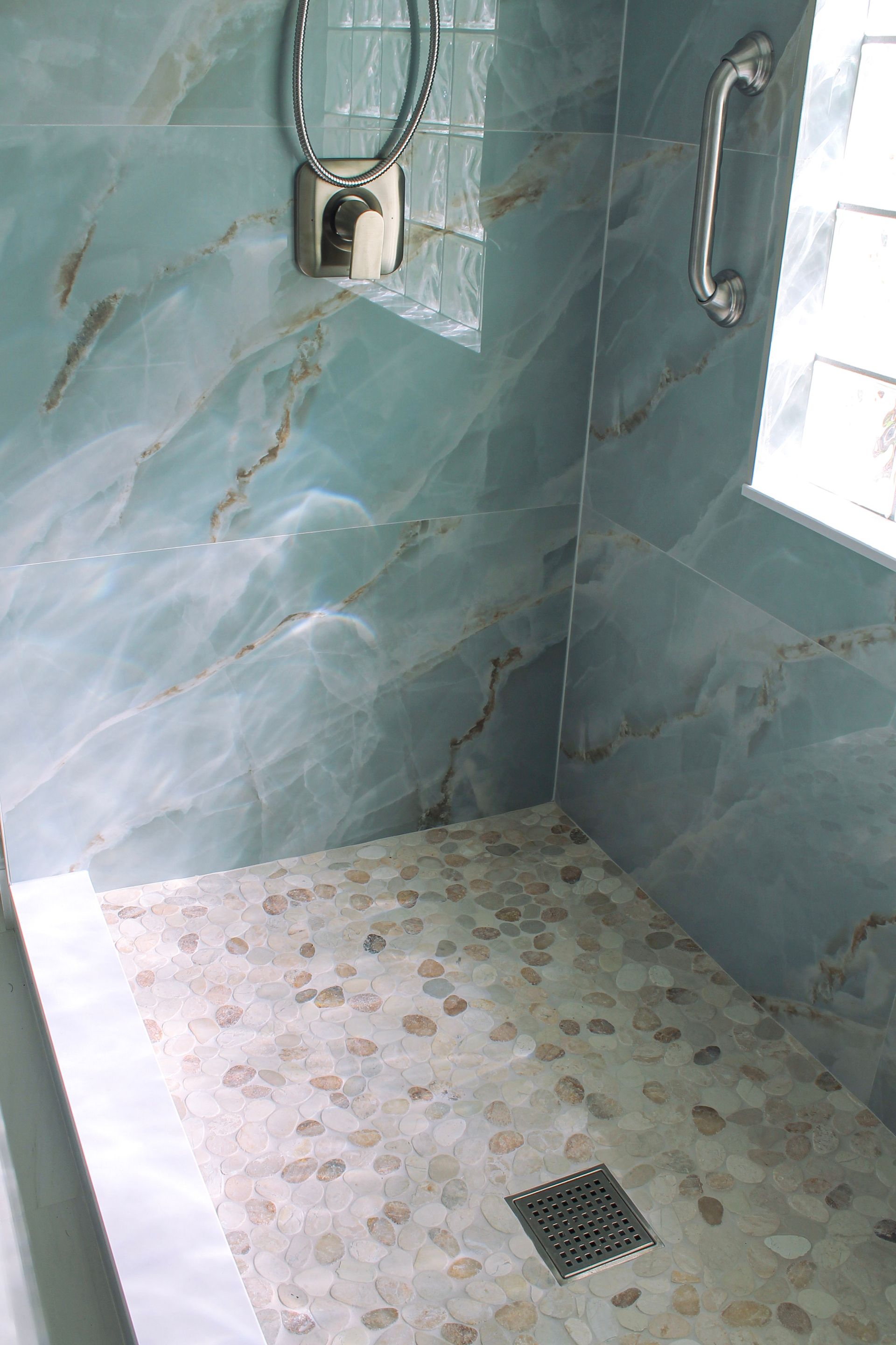 Modern blue tile bathroom with glass block window, white grout, Niche with white trims and mosaic, modern mosaic flooring with white grout and brushed stainless steel accessible handle and brushed stainless steel drain pebble mosaic flooring