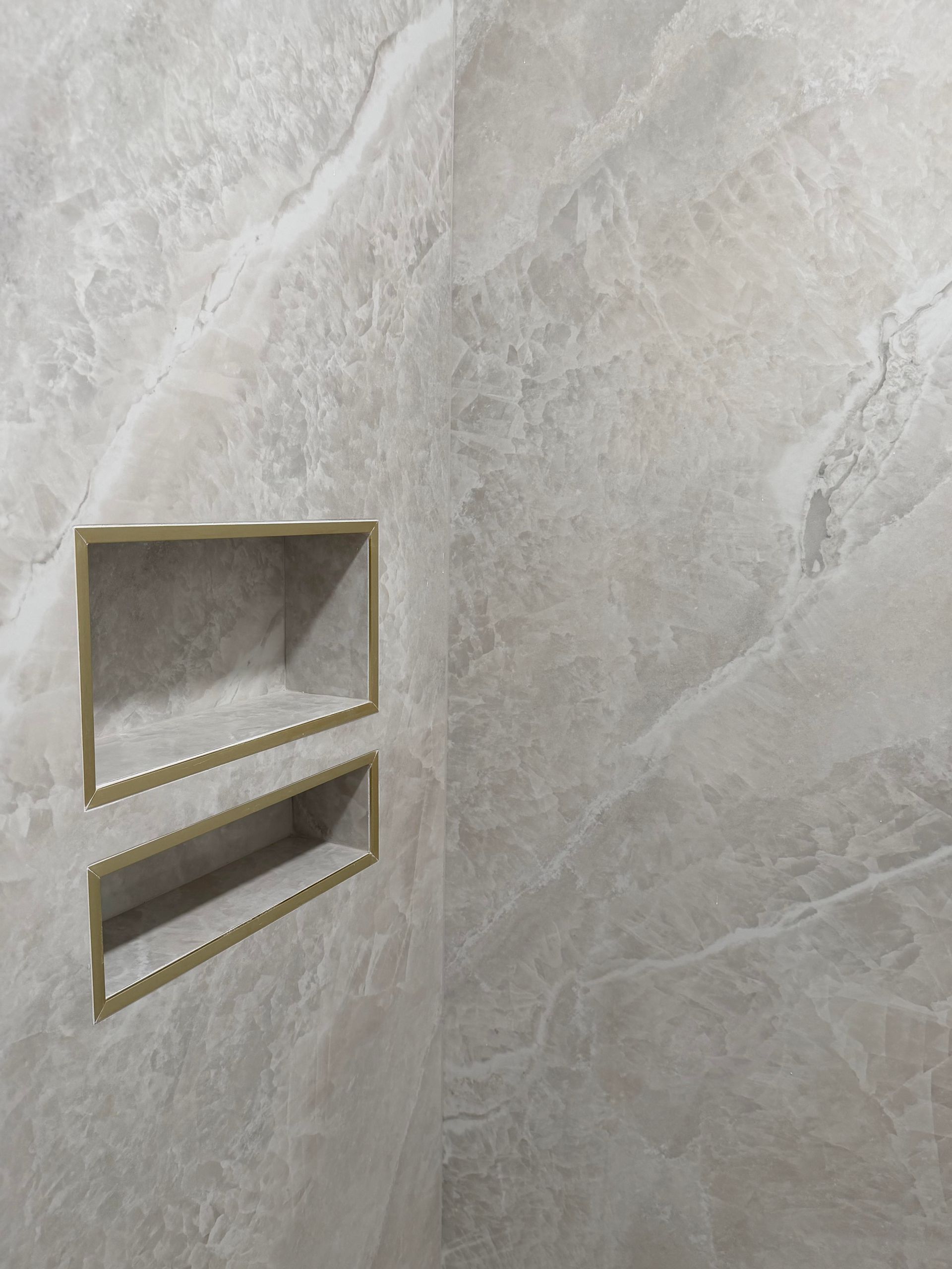Two recessed gold-trimmed wall niches in a light gray stone-tile wall