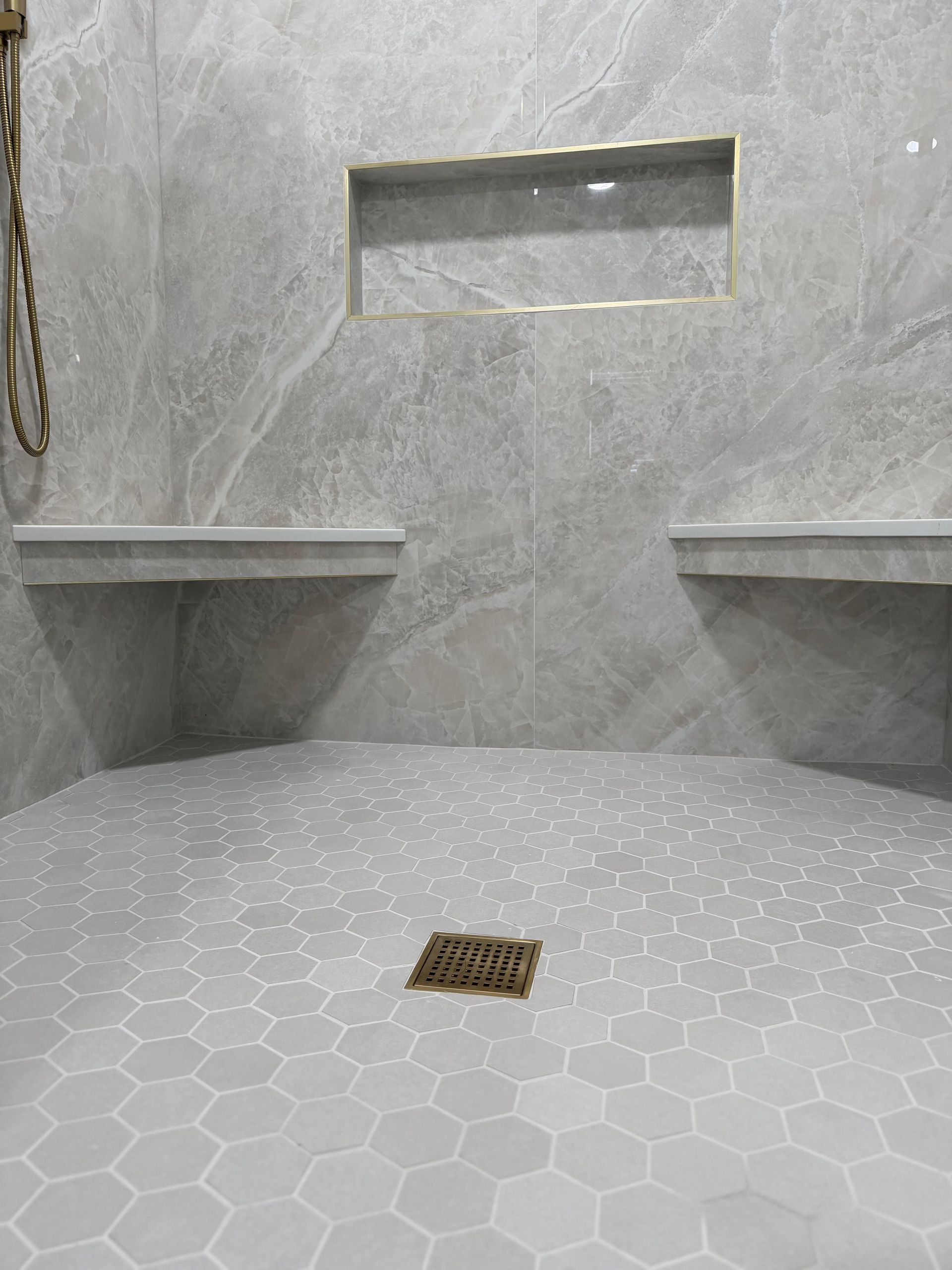 Symmetrical dual luxury tile shower, large format 110''x48'' grey matte tile, with built in niche, dual shower heads , dual tile and quartz bench, large niche, luxury floor with brushed gold hardware