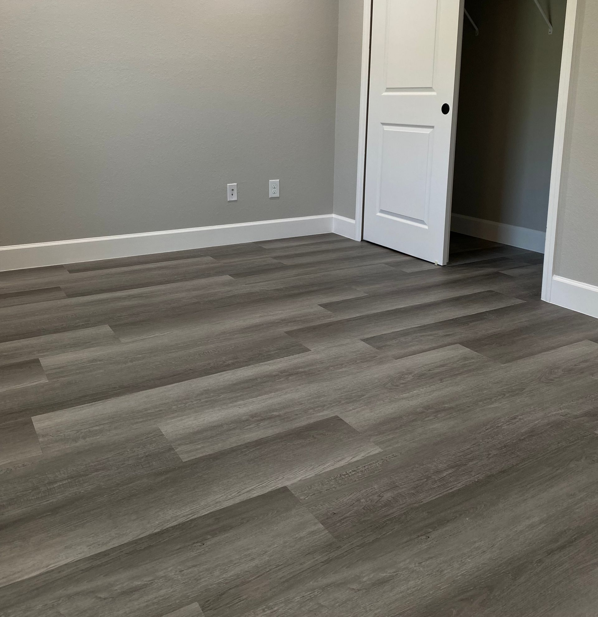 Dark grey wood look spc vinyl flooring in a room with light grey walls and white baseboards and white closet doors
