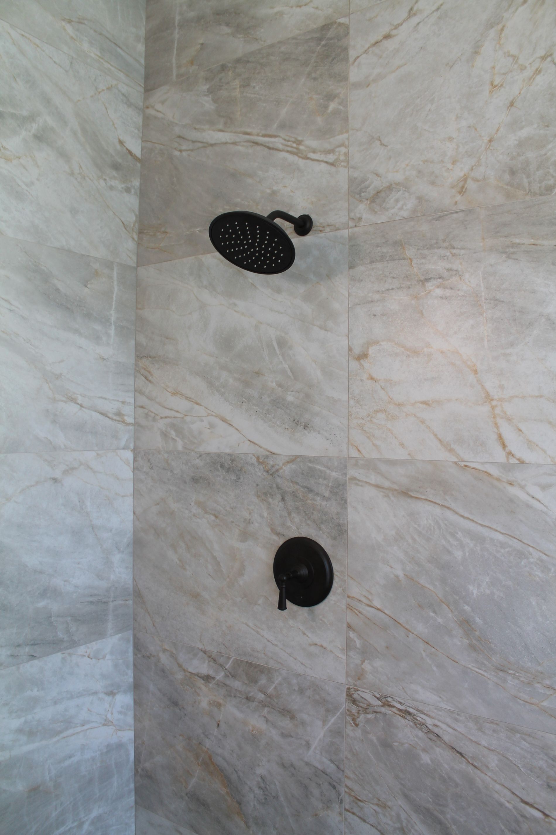 Two black shower fixtures on a gray marble-tiled wall
