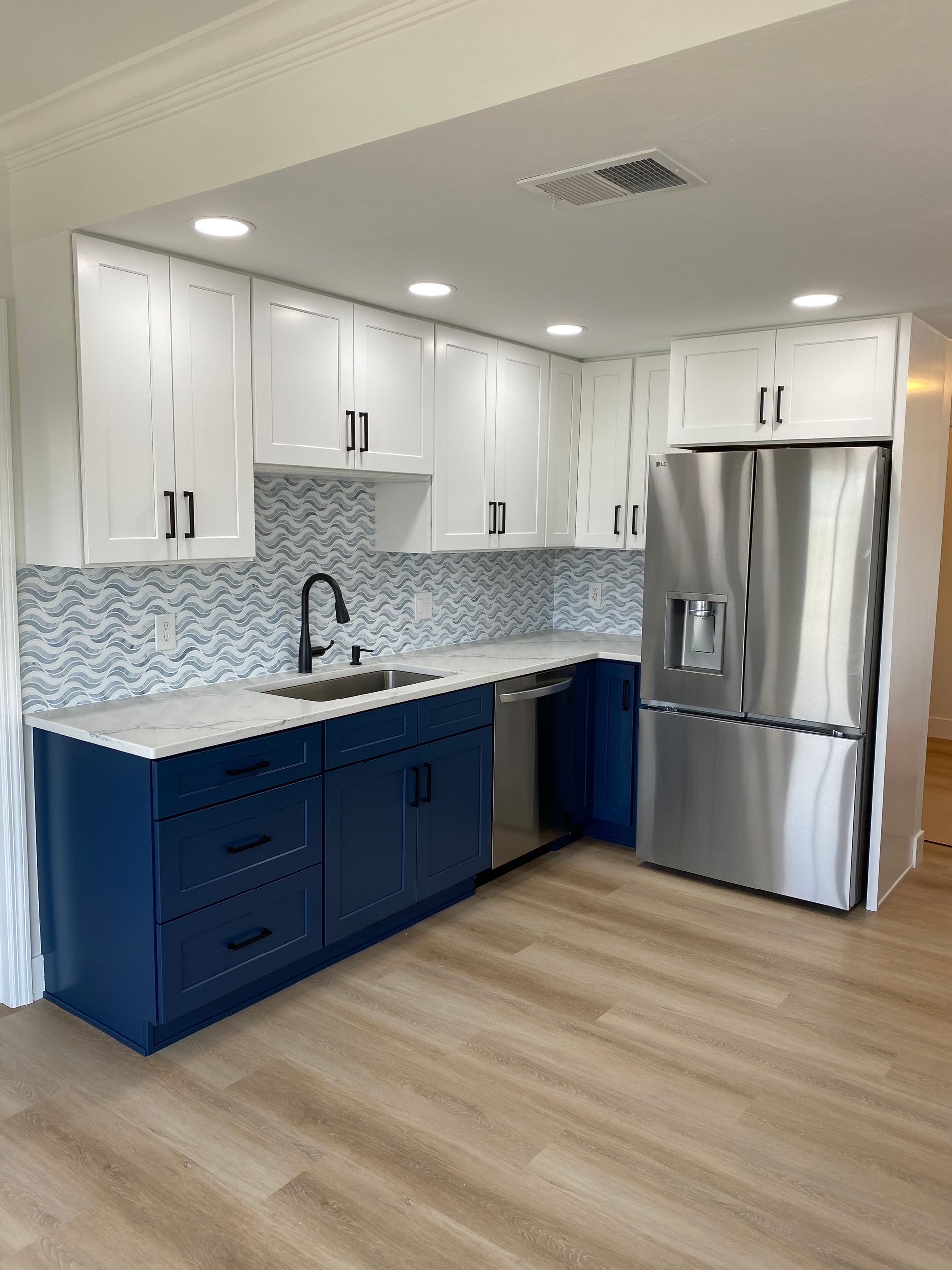 Modern kitchen with blue cabinets, tan light vinyl flooring brushed stainless steel accents and trim, double door fridge and blue backsplash