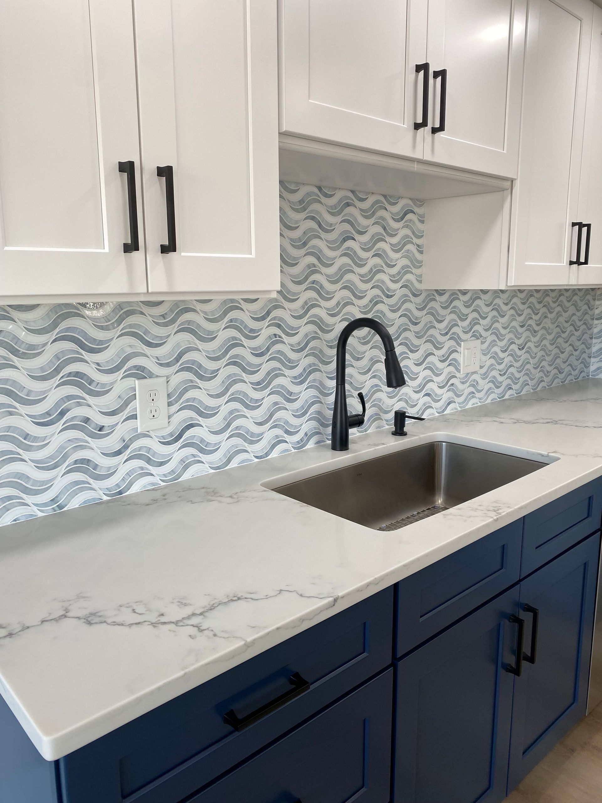 Modern kitchen with white cabinets, blue lower cabinets, marble countertop, and stainless sink with black faucet