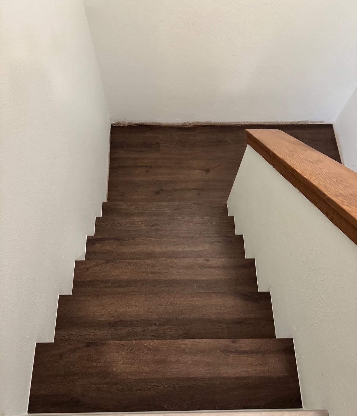 A wooden staircase with a white wall and a wooden railing
