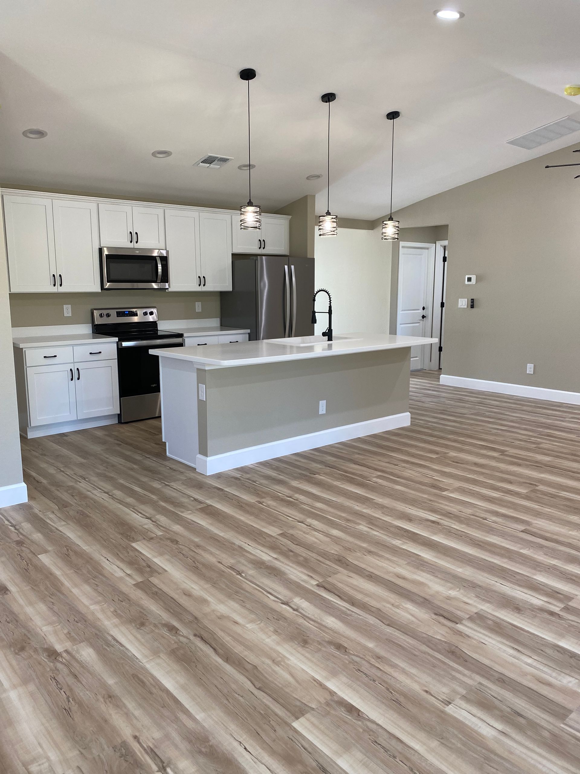 An empty kitchen with hardwood floors and white cabinets