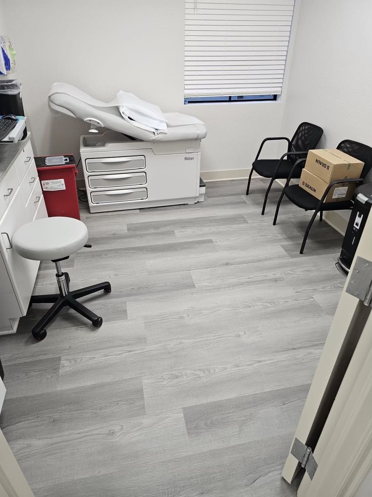 A doctor 's office with a bed , chairs , and a box on the floor.