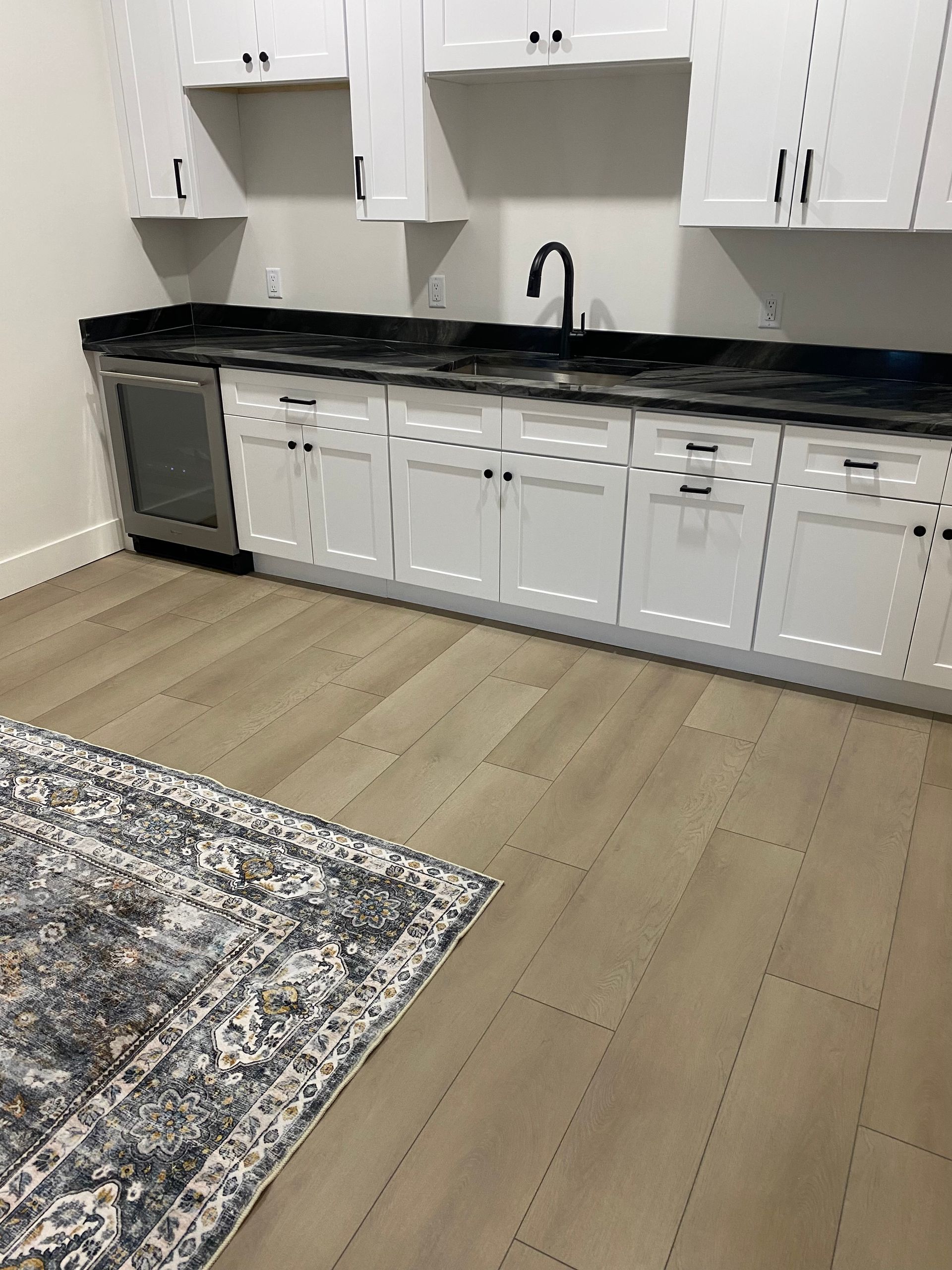 White shaker cabinets with matte black accents and tap as well as black countertop with beige vinyl flooring
