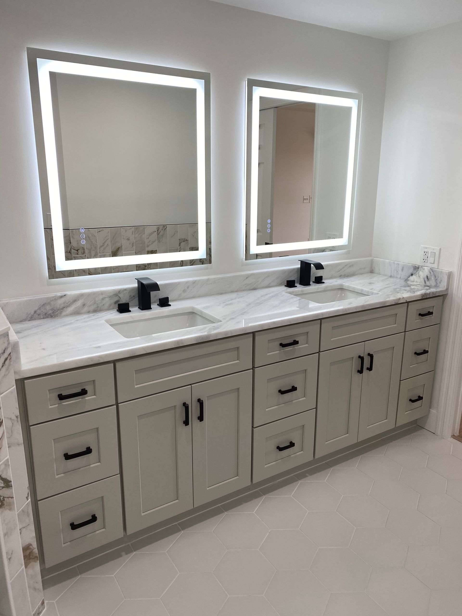 Modern double vanity bathroom with marble countertop, backlit mirrors, and gray cabinets