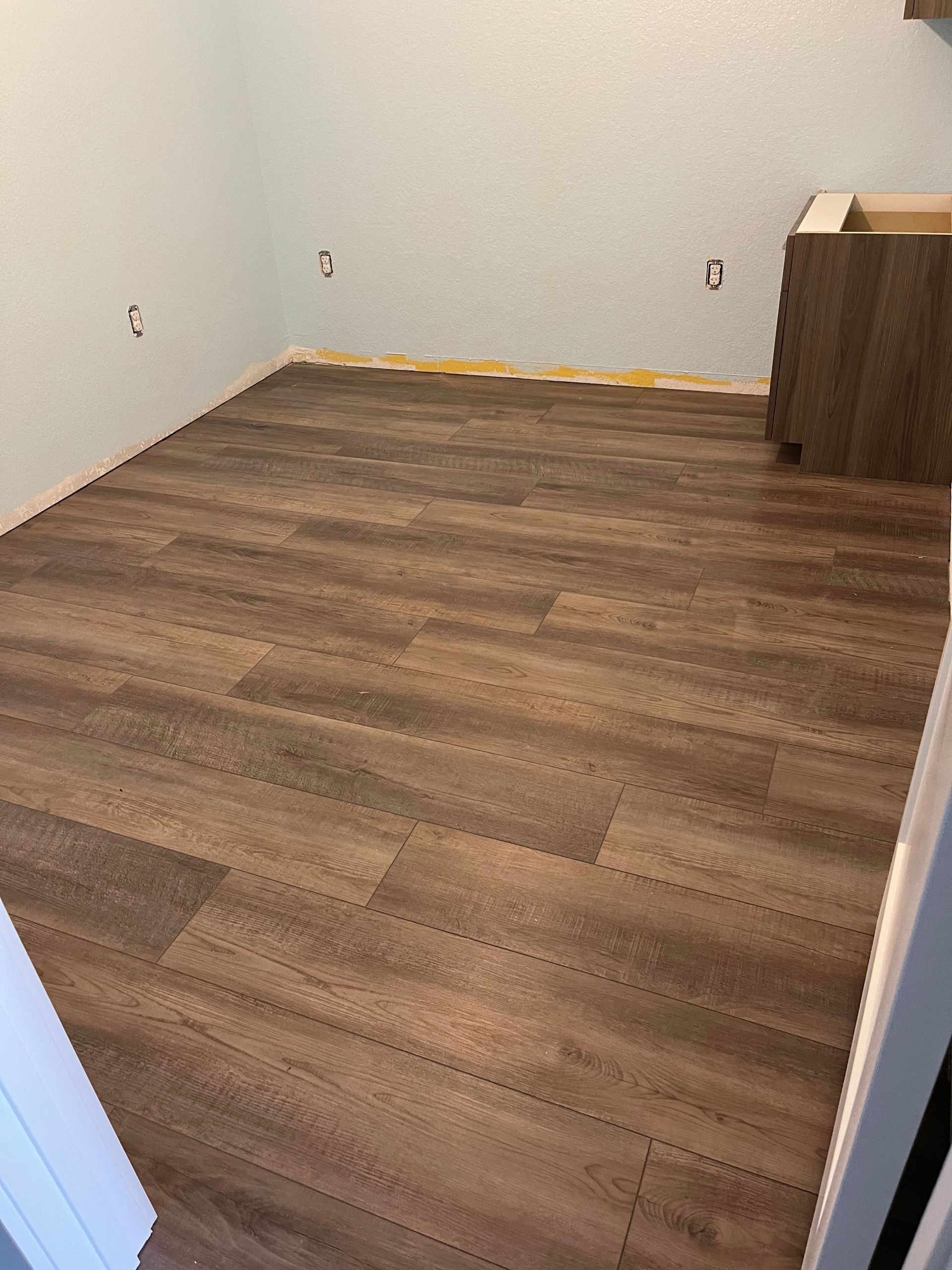 Room with brown wood-look flooring, light blue walls, and cabinet partially installed.