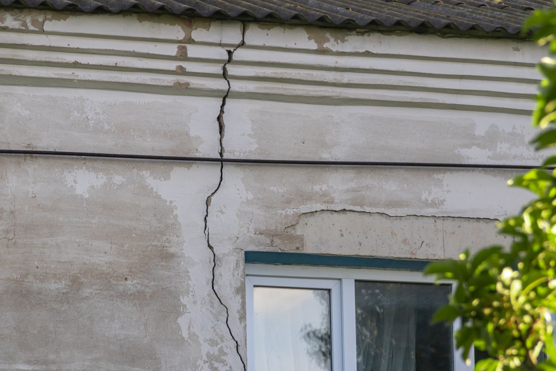 Large deep vertical crack on the old concrete stucco facade of a residential house wall. Large deep vertical crack on the old concrete stucco facade of a residential house wall.