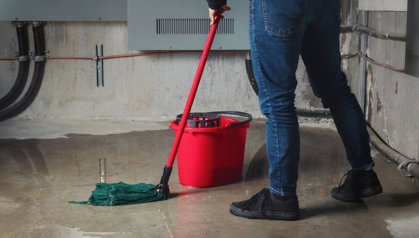 Person mopping a wet concrete floor with red mop and bucket.