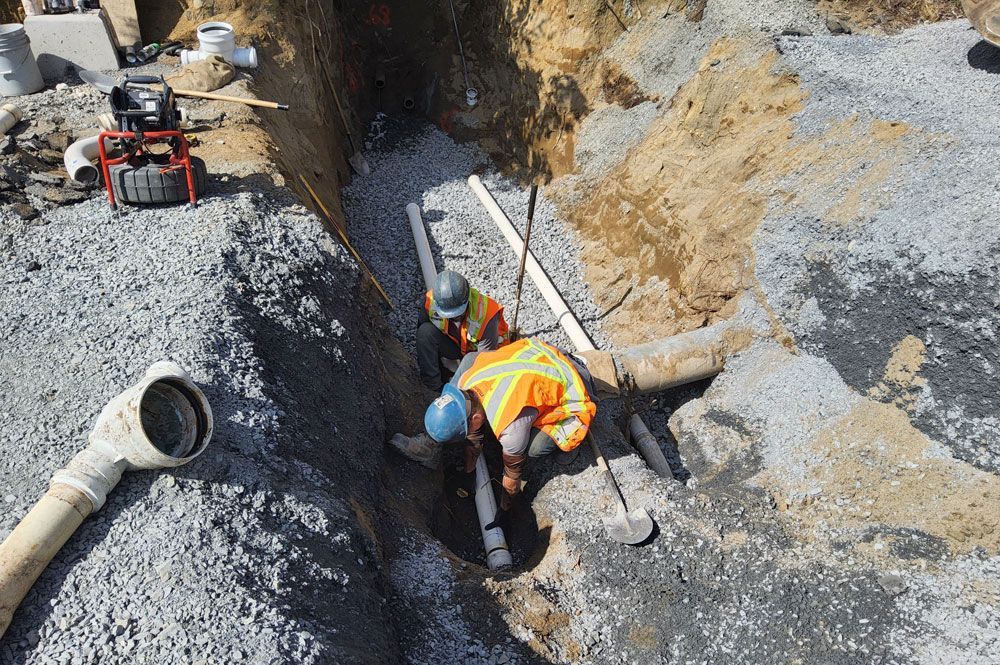 Workers in orange vests digging a trench beside large pipes at a construction site