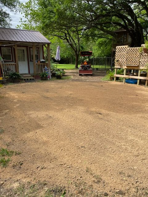 Open dirt courtyard with trees, a small building on the left, and a raised bamboo platform on the right