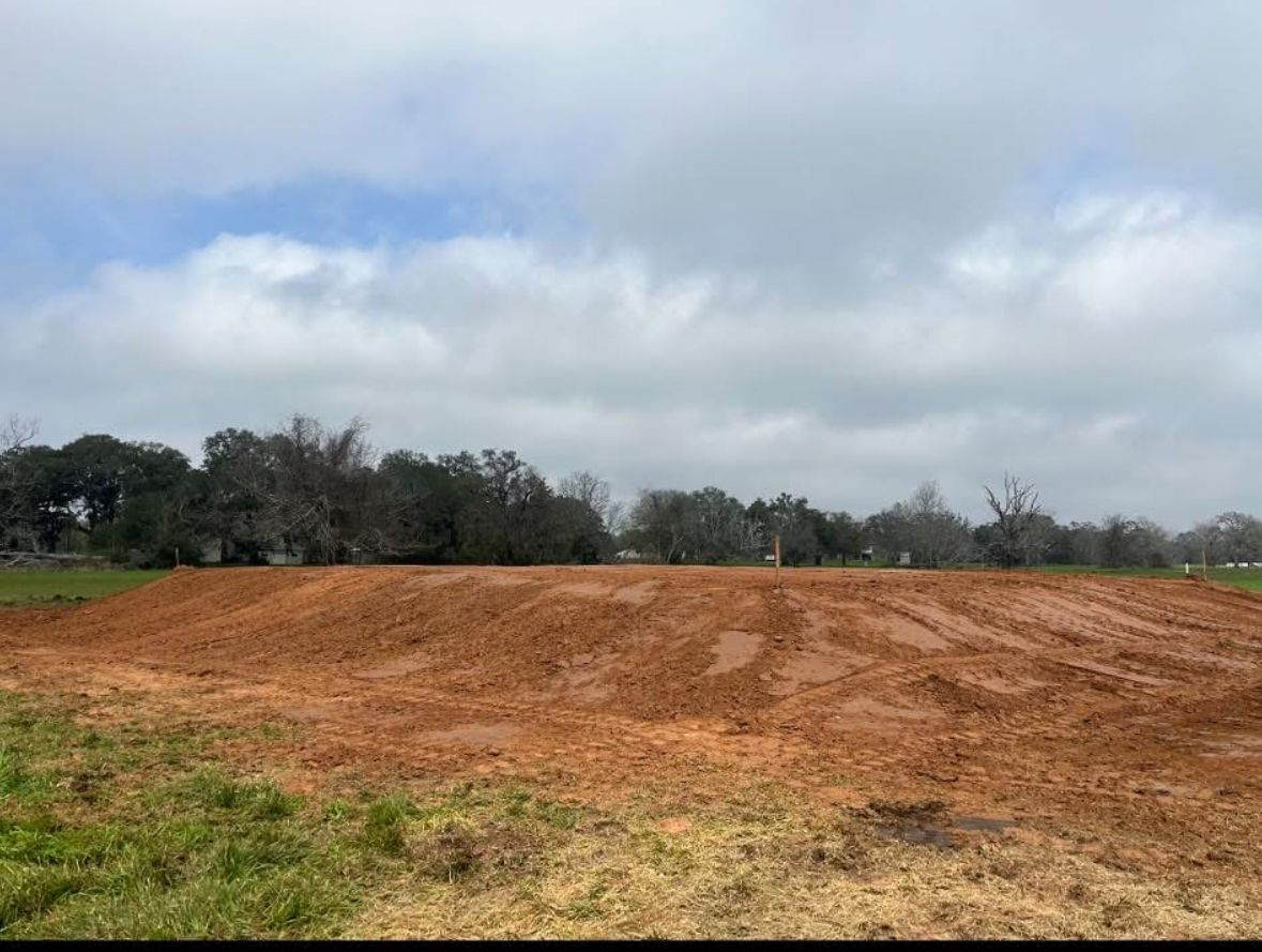 A dirt mound with tire tracks in front of a tree line under a cloudy sky.