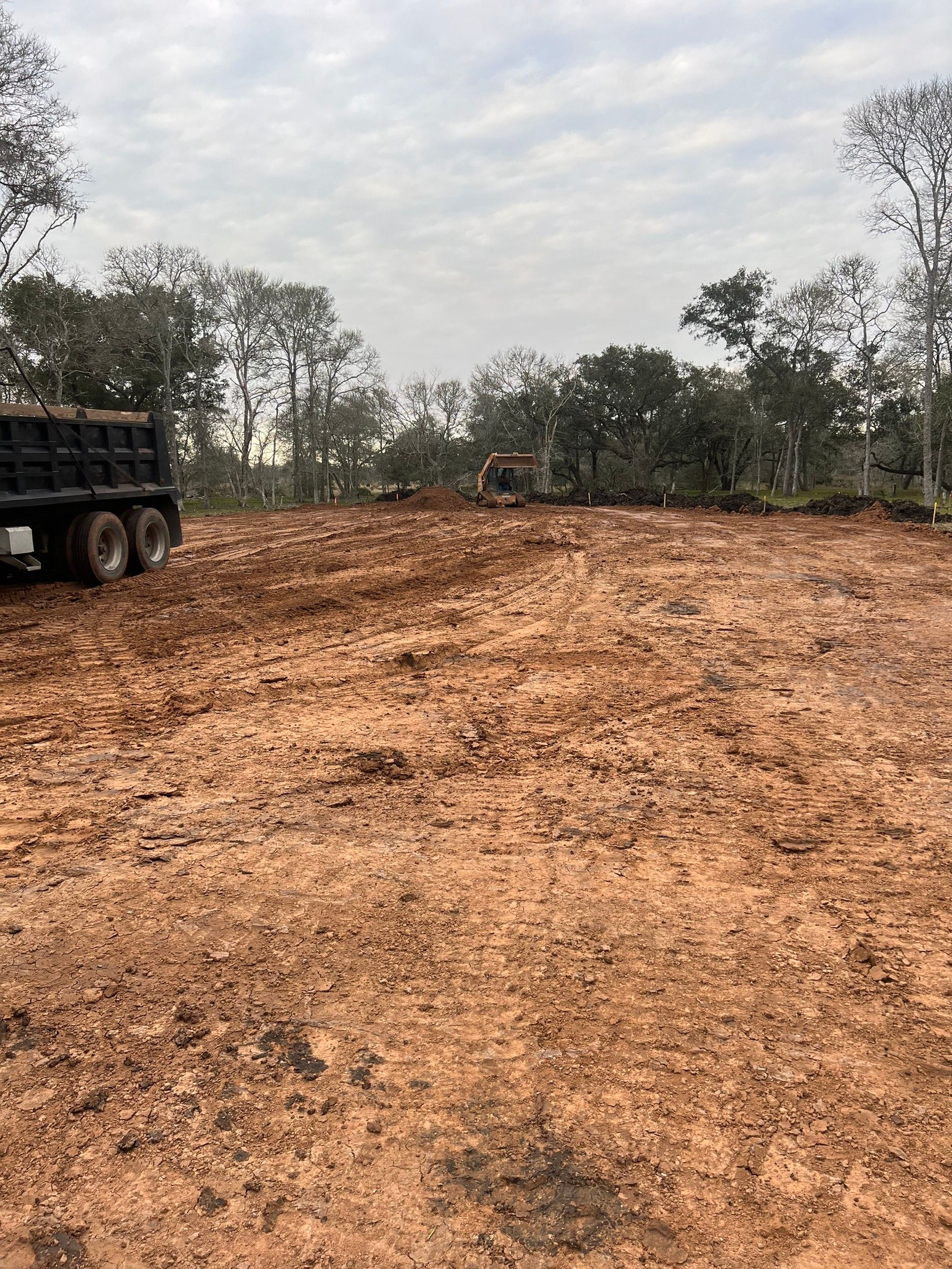 Cleared dirt lot with truck on left, trees in background, cloudy sky.