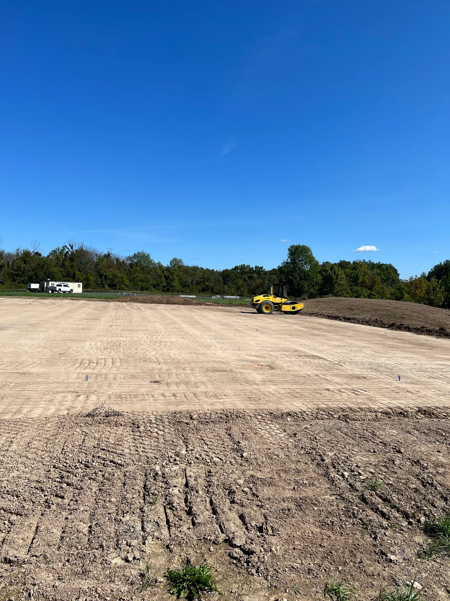 A cleared construction site under a clear blue sky, with a yellow compactor machine visible.
