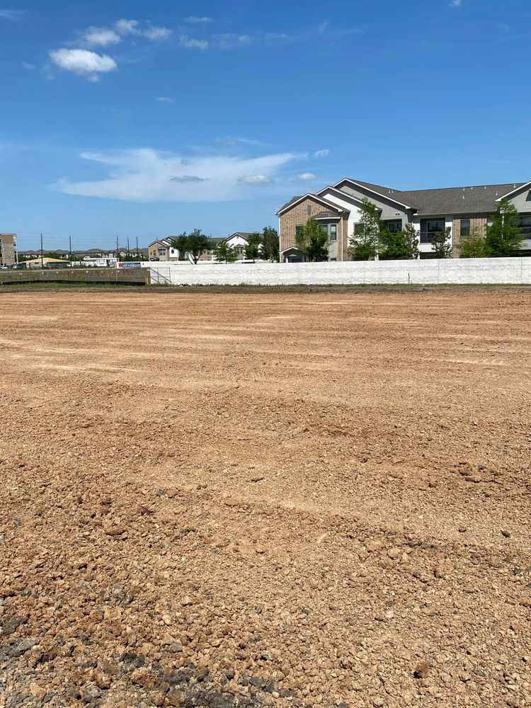 Cleared lot with brown dirt, white wall, and apartment buildings under a blue sky.