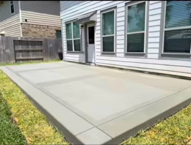 Concrete patio with a house in the background. Grass and a wooden fence surround it.