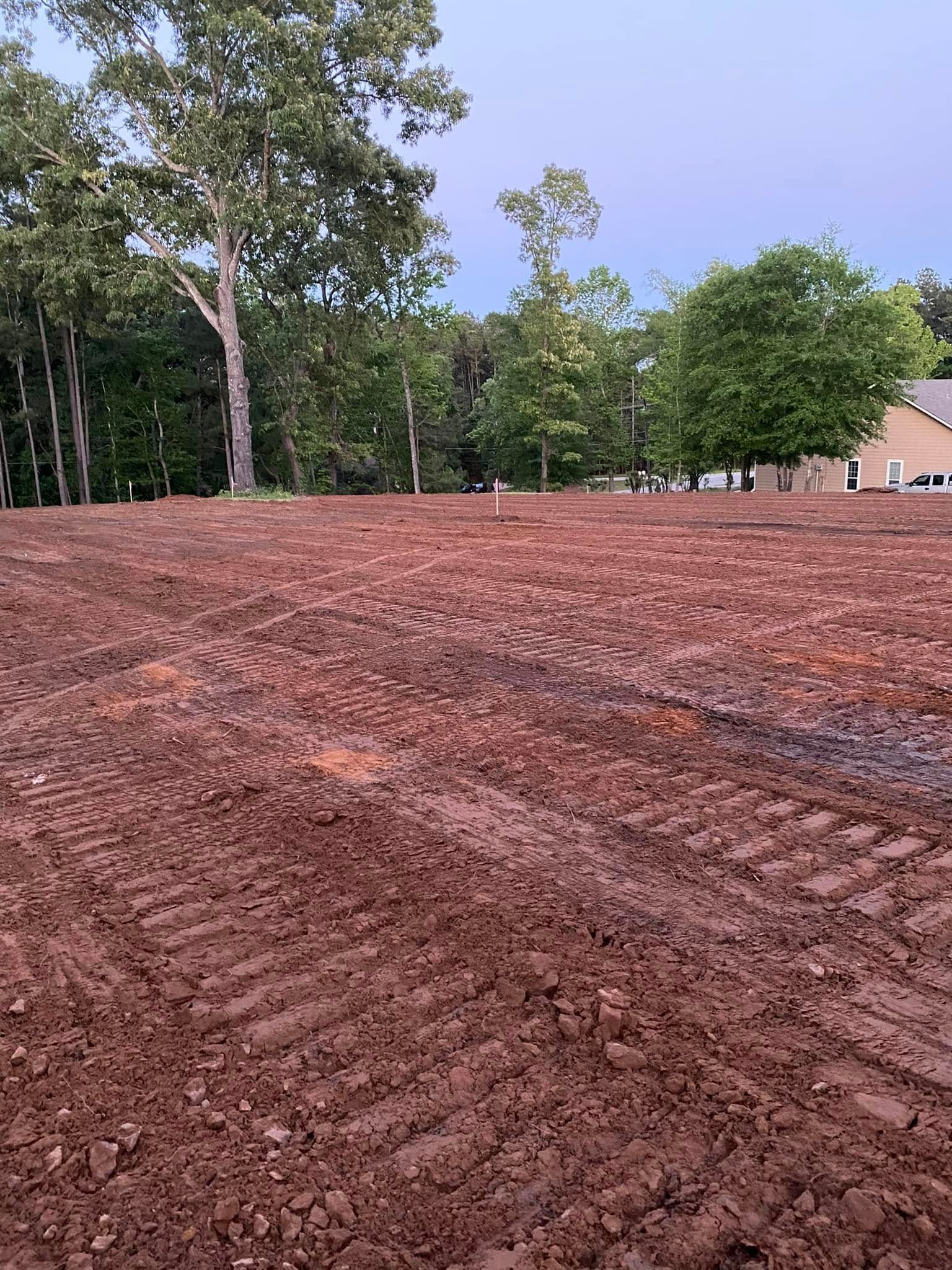 Dirt field with tire tracks, trees in the background, possibly a construction site.