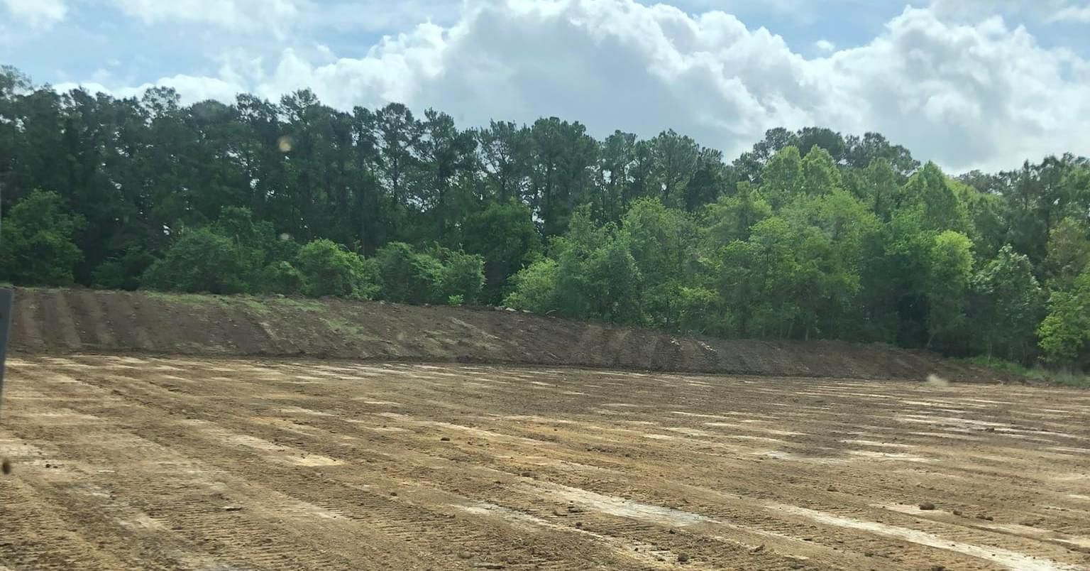 Brown dirt field with a tree line in the background under a cloudy sky.
