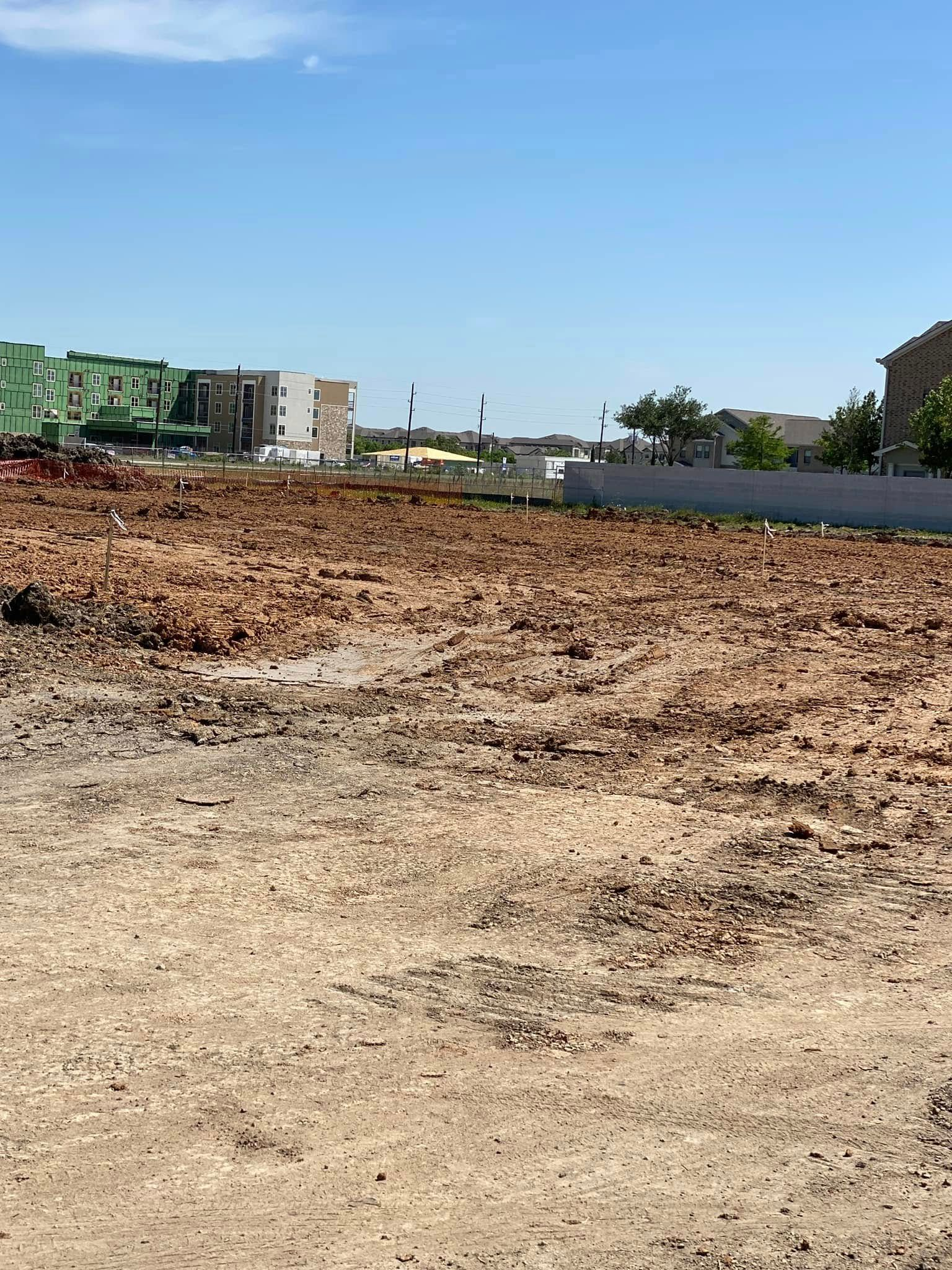 Cleared construction site with dirt and debris, buildings in the background under a blue sky.