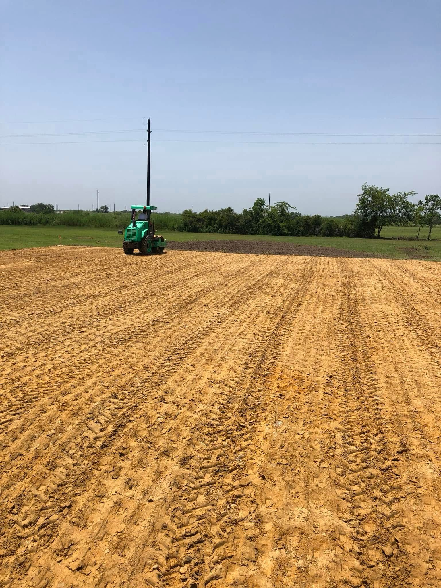 A small green tractor on a tilled field under a clear sky.