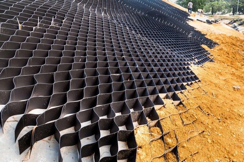 Black honeycomb-like structure covering a slope of dirt, likely for erosion control.