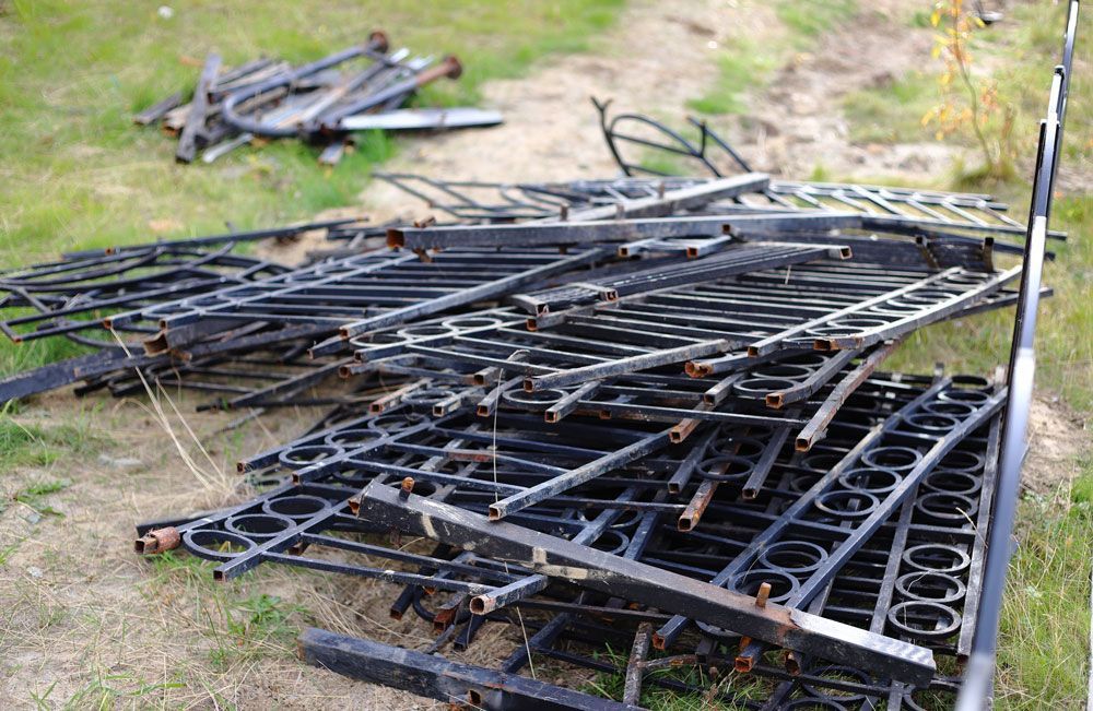 Bent black metal fence sections and rods piled on grass outdoors