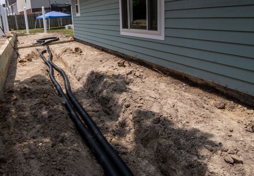 Black cables run through a dirt trench beside a blue house under construction.