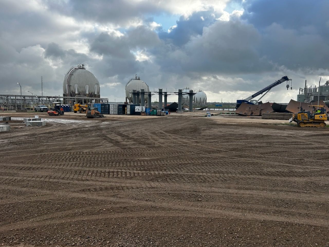 Construction site with tanks, heavy machinery, and dirt under a cloudy sky.