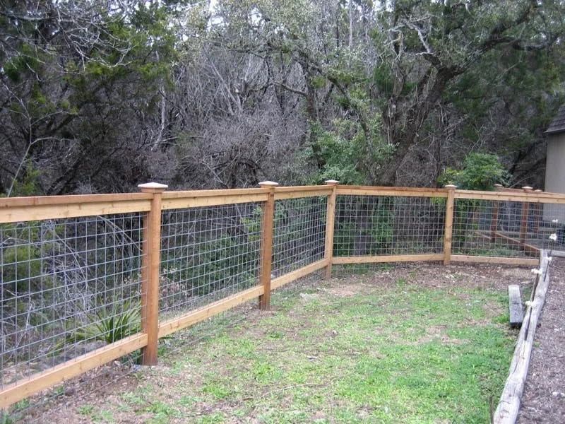 Wooden wire fence along a grassy yard beside dense trees and a house wall