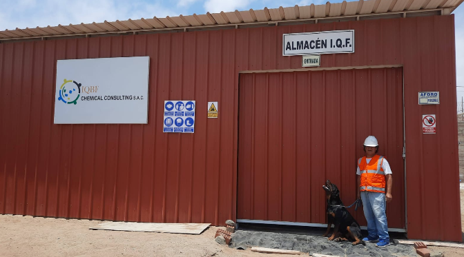 Una persona con chaleco de seguridad y casco está de pie con un perro frente a un almacén