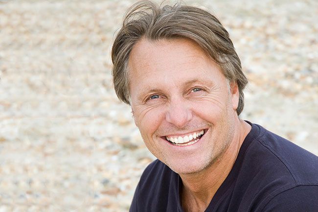 a man is smiling for the camera while sitting on the beach .