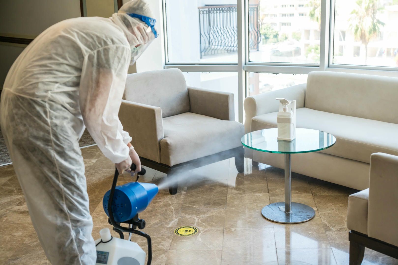 A man in a protective suit is disinfecting a living room.