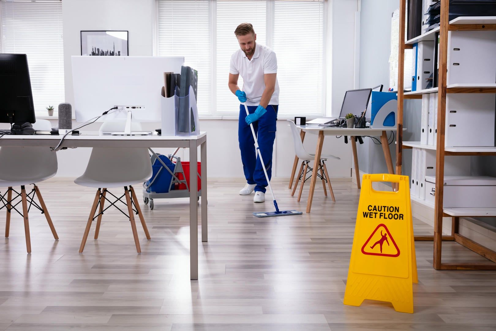 A man is mopping the floor of an office next to a caution wet floor sign.