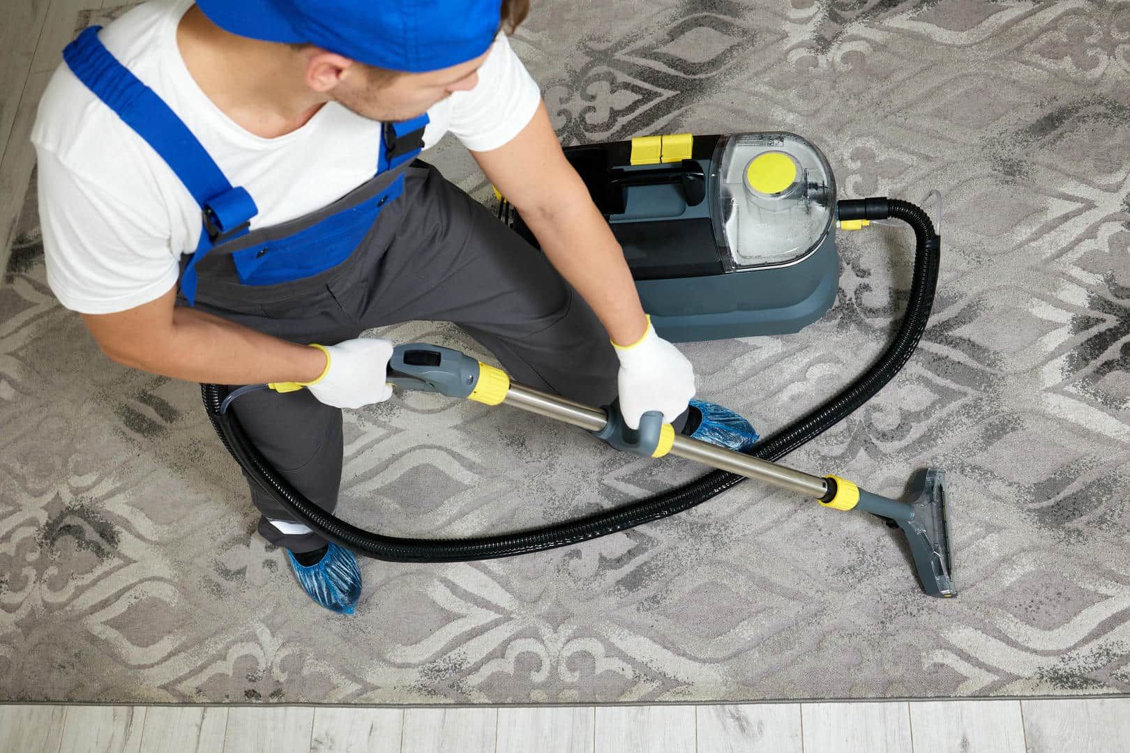 A man is cleaning a rug with a vacuum cleaner.