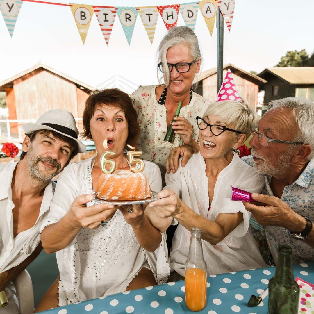 Group of older adults celebrating a birthday with a cake and candles, outside.