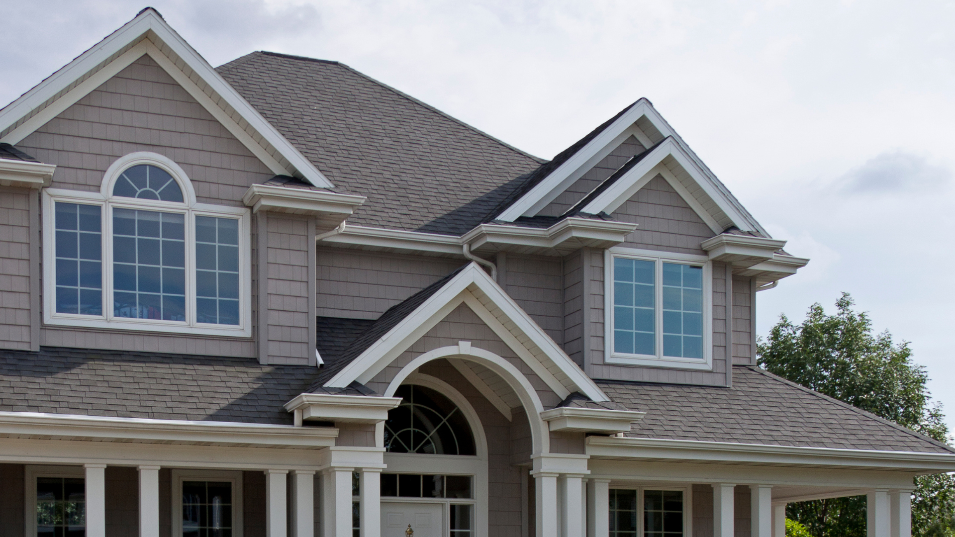 Suburban house with gray siding, white trim, arched entry, and large windows