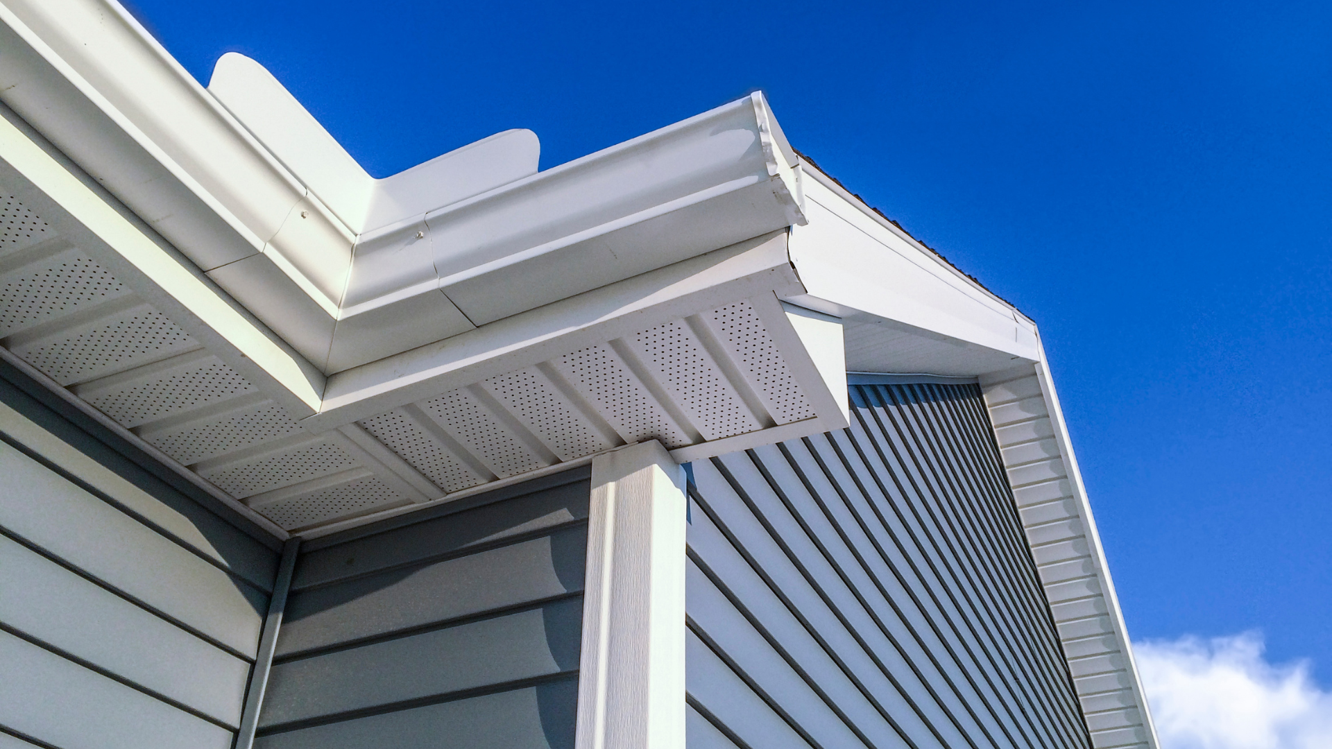 Close-up of house eaves with white trim, gray siding, and blue sky above