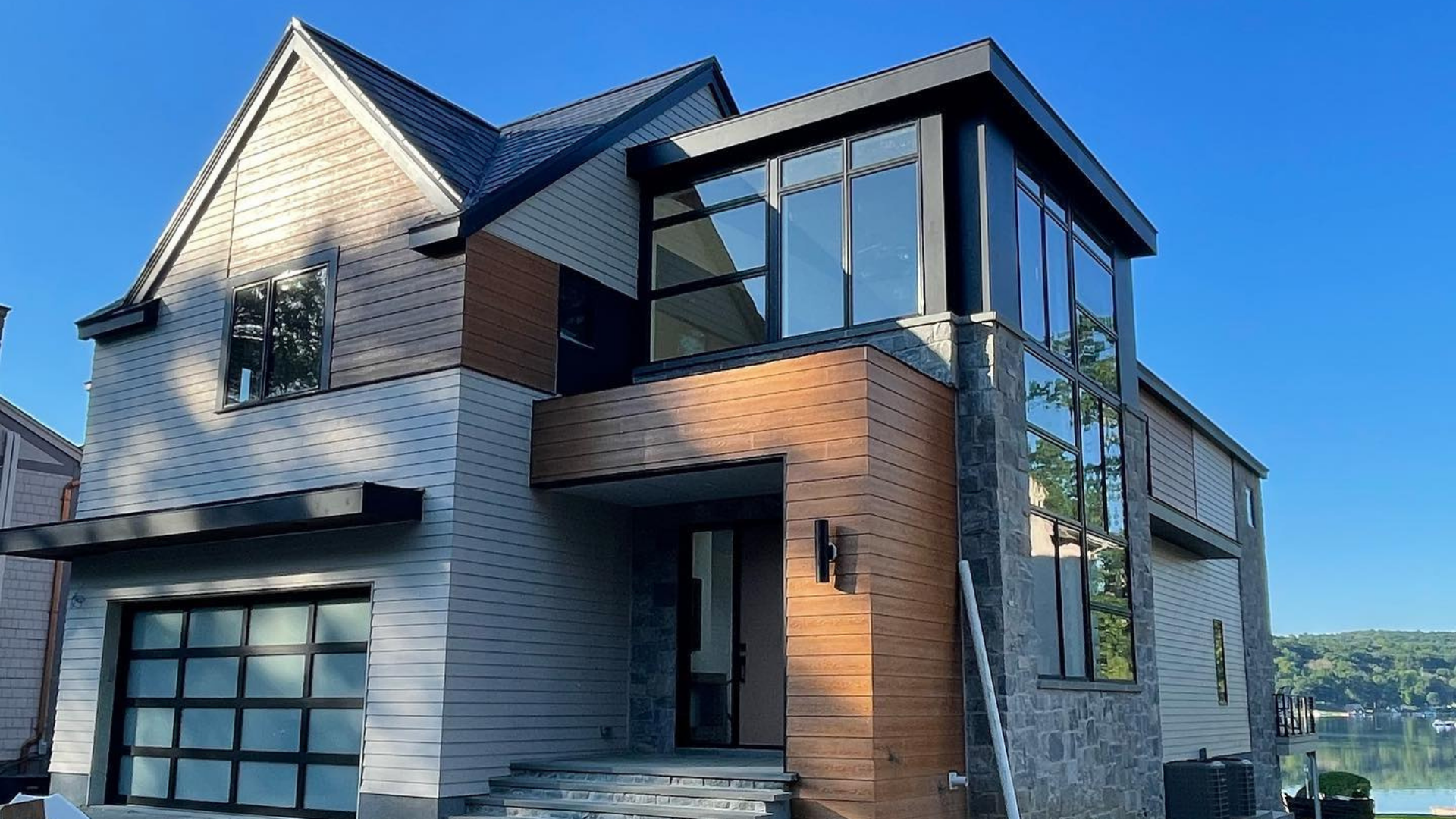 Modern two-story house with brick and gray siding, large windows, and a sloped roof in a sunny setting