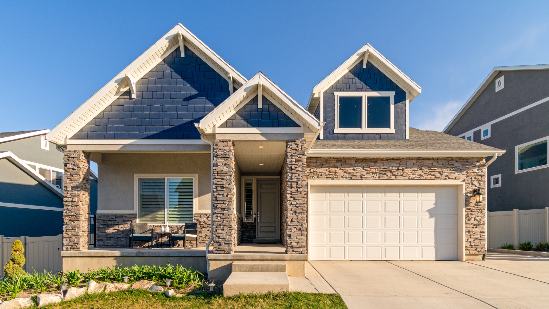Single-story brick house with gabled roof, front porch, and white garage under a blue sky
