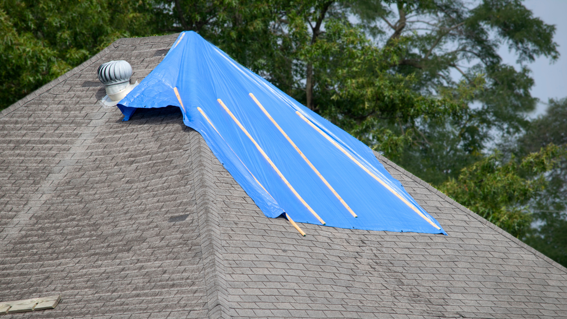 Blue tarp covering storm-damaged roof section on a house