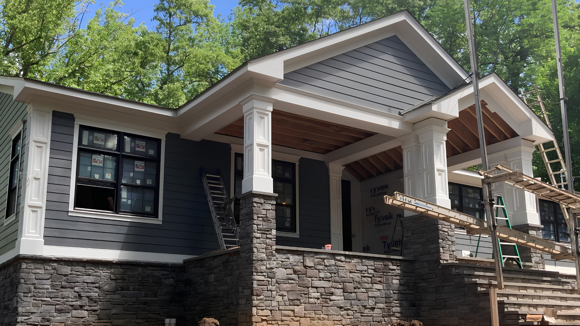 Partially renovated gray house with stone porch columns and construction scaffolding on the right