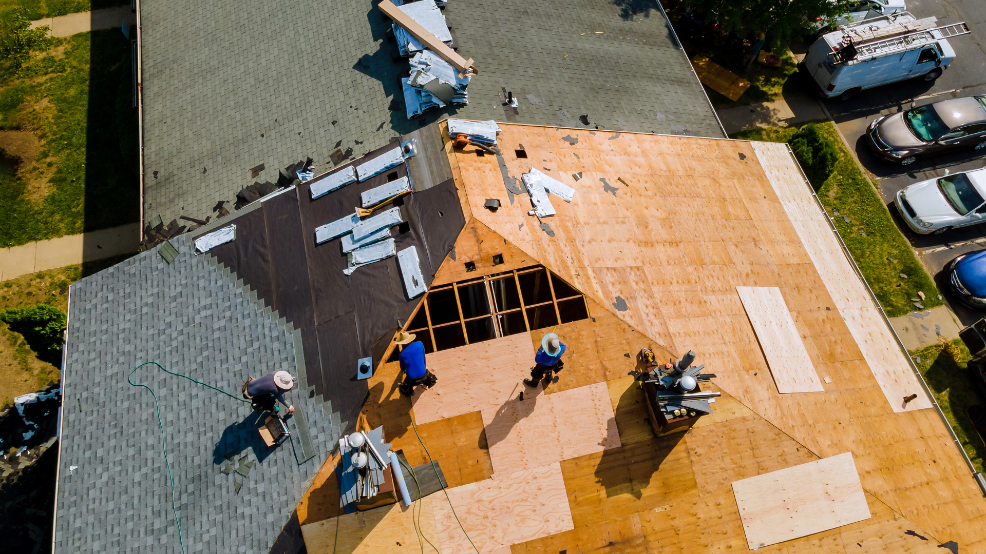 Roofing crew repairing a house roof with exposed plywood and scattered materials