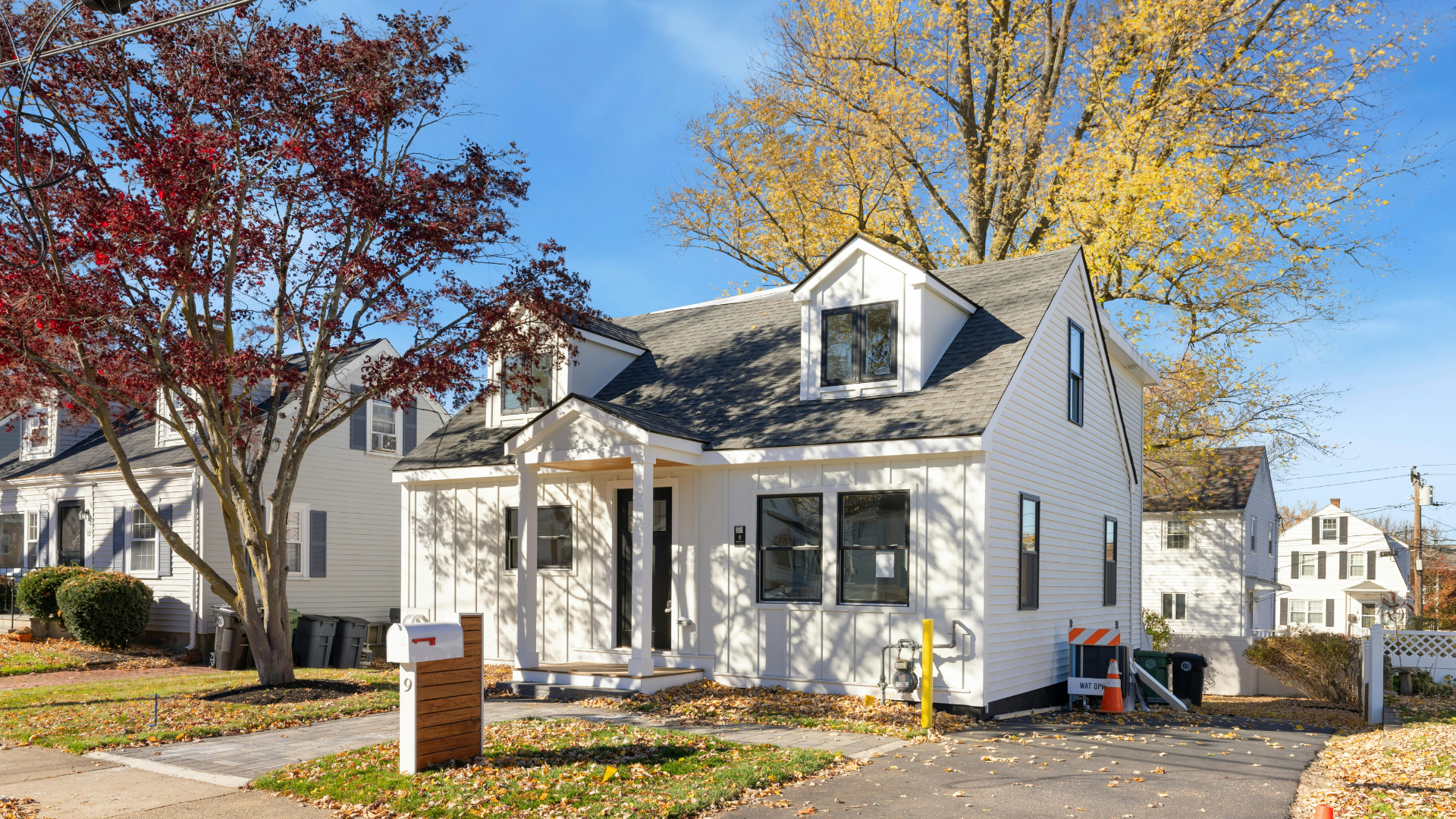 White house on a tree-lined street with autumn leaves and a sidewalk construction barrier
