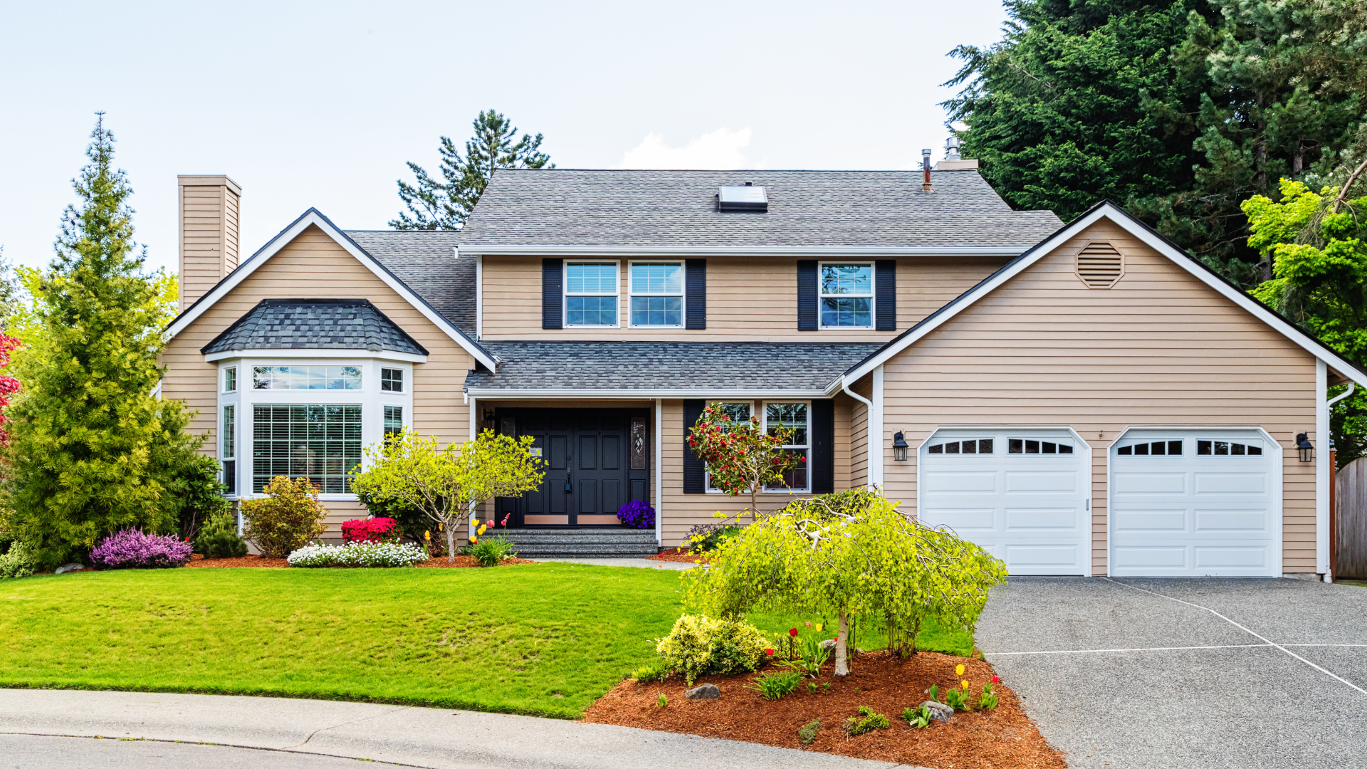 Suburban beige house with blue shutters, two-car garage, front lawn, and landscaped garden