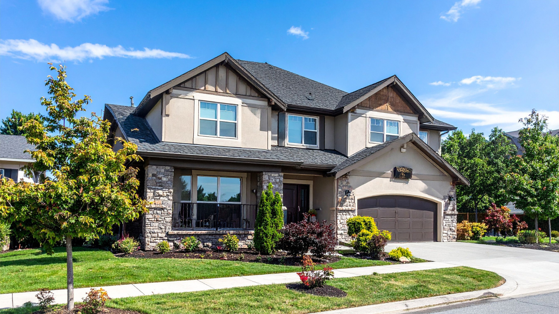 Two-story suburban house with a gray roof, brick facade, garage, and a manicured front lawn under a blue sky